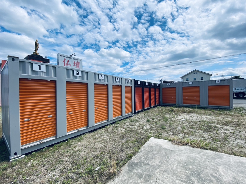 屋外に並んだコンテナ型トランクルームの前に車を停め、段ボールに入った備蓄品を積み込んでいる男性