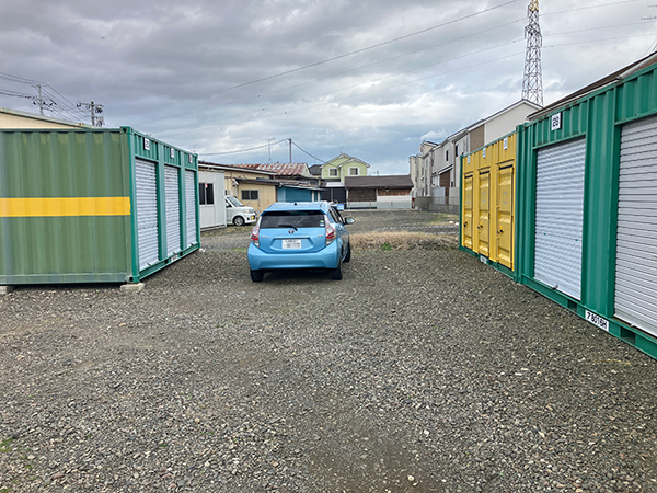 屋外コンテナ型トランクルームの前に車を横付けし、シャッターを開けて荷物を積み込む家族の様子