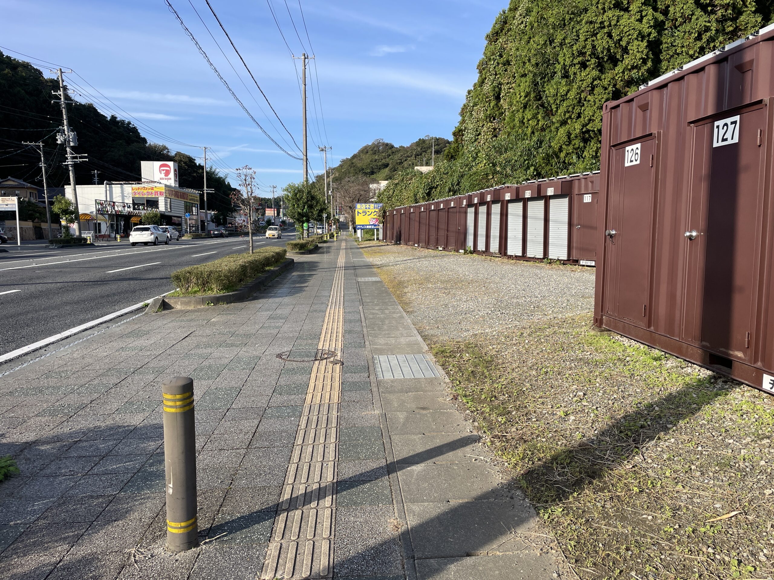 屋外に並んだシルバーのコンテナ型トランクルームの前に車を停め、シャッターを開けてキャンプ用品を積み込む父親