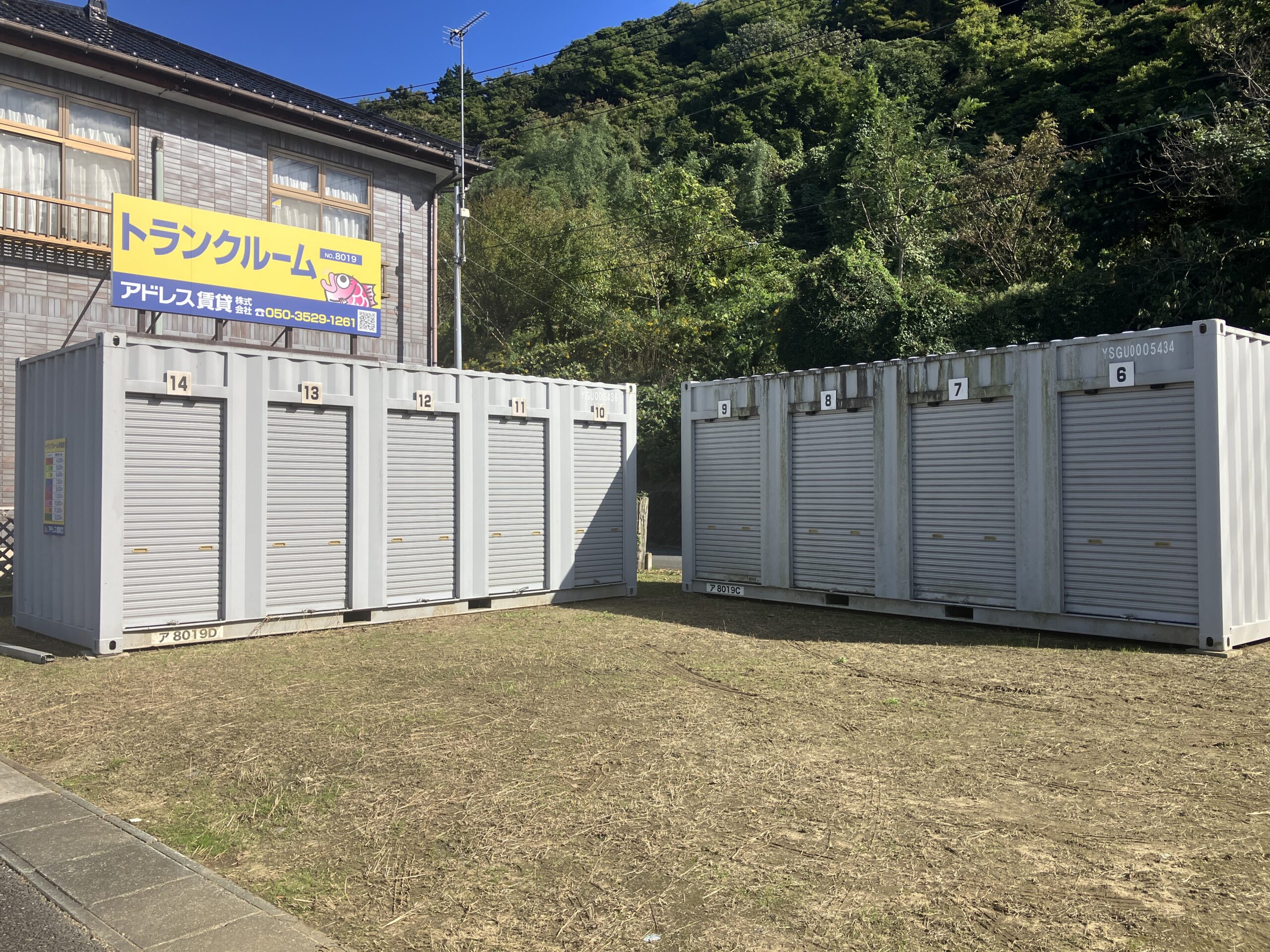 屋外に並ぶシルバー色のコンテナ型トランクルームの前で、スマートフォンを片手に契約完了メールを確認する男性