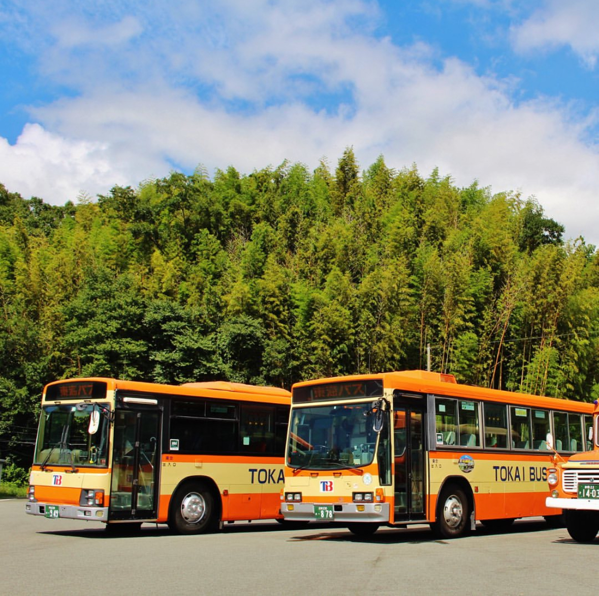 東海バスの営業所に出勤し、運行管理者に笑顔で出勤報告をするバス運転士。清潔な制服姿で、背景には整備されたバスと朝の青空が広がる