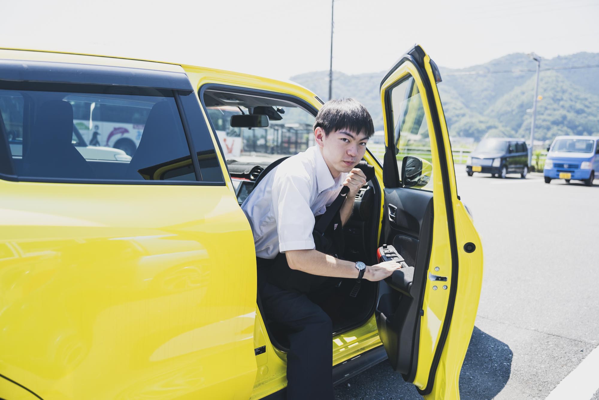 伊豆半島の営業所の駐車場に並ぶ社員のマイカーと、その奥に見える路線バスの車庫