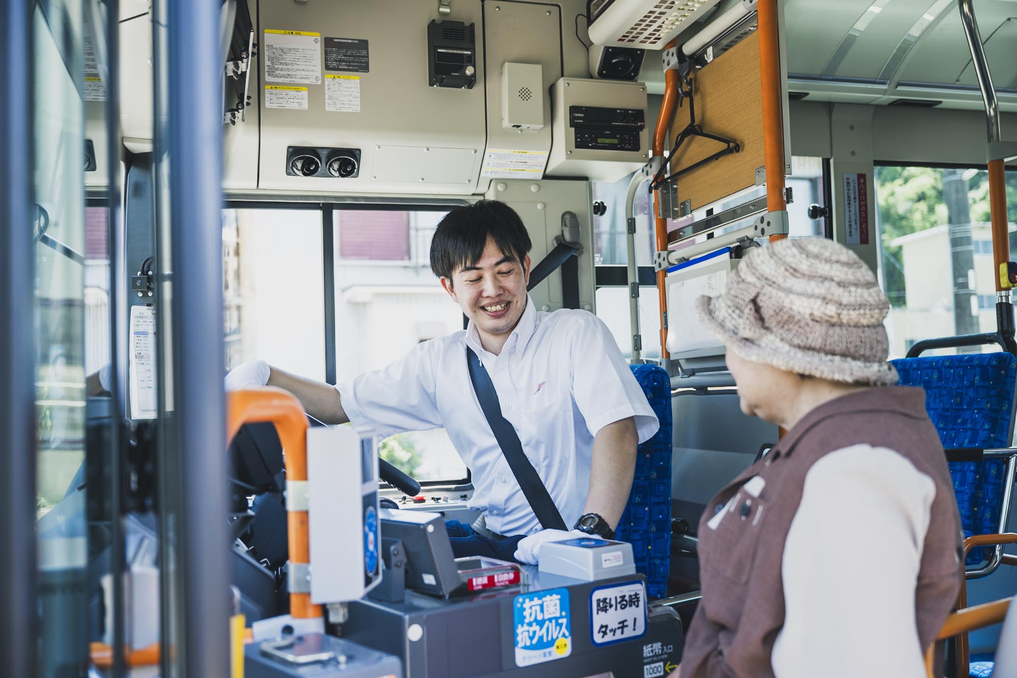 バスの運転席で笑顔で乗客に挨拶をする正社員の女性運転士