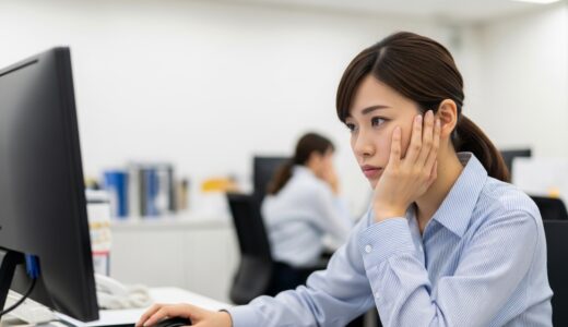 夜遅くまで残業するオフィスで、疲れた表情でパソコン画面を見つめる女性