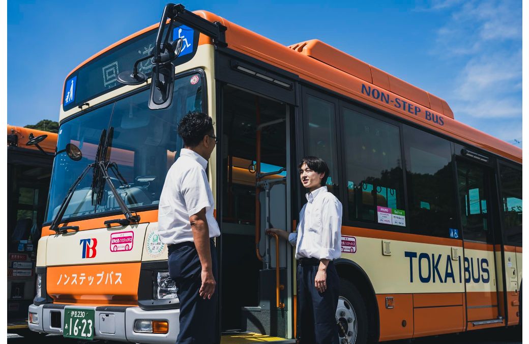 青空の下で健康的な笑顔を見せるバス運転士たち（男女混合）が休憩所で談笑している様子