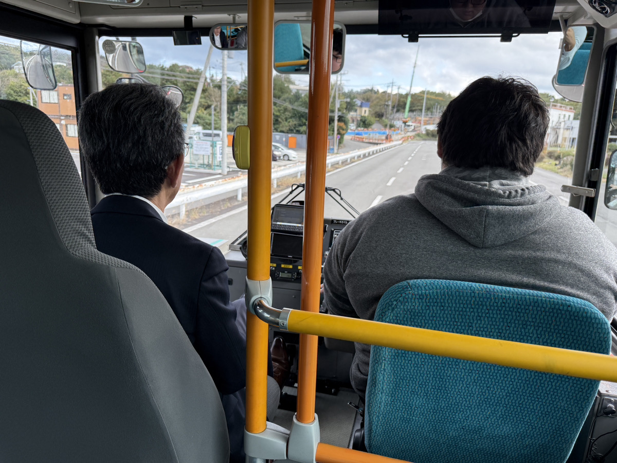 バス車庫で実際のバスの運転席に座って説明を受ける参加者と、横で優しく教える指導員