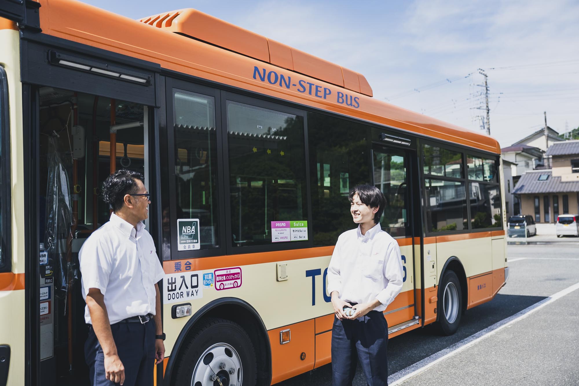 明るい表情でバスの運転体験会の説明を聞く、カジュアルな服装の参加者たち