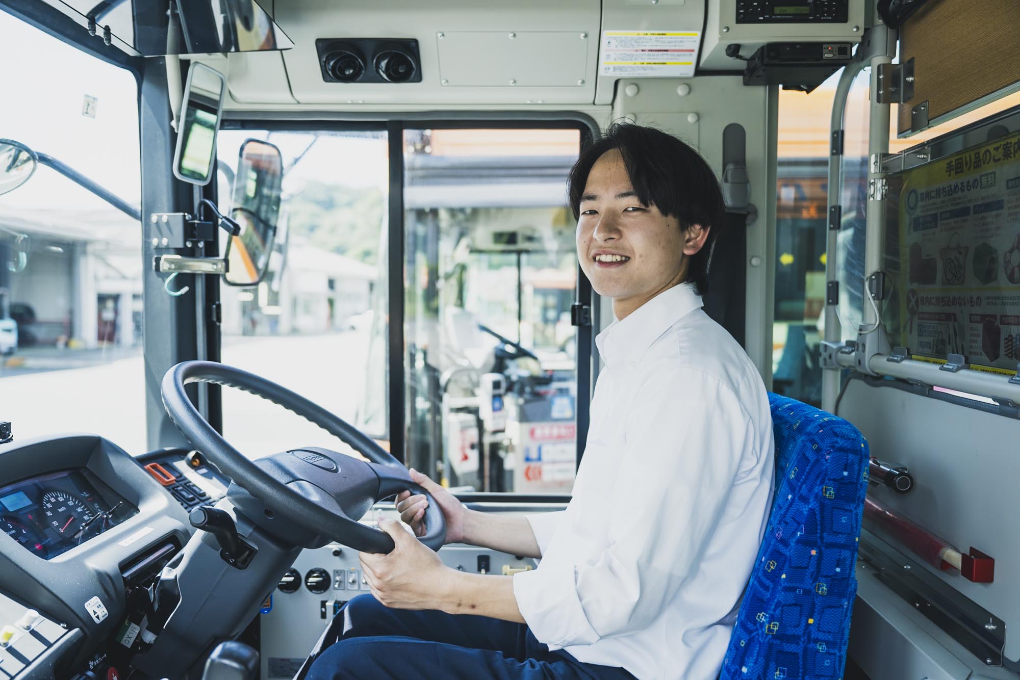 制服を着て明るい表情で運転席に座る30代のバス運転士、清潔なバス車内、誇りと安心感のある雰囲気