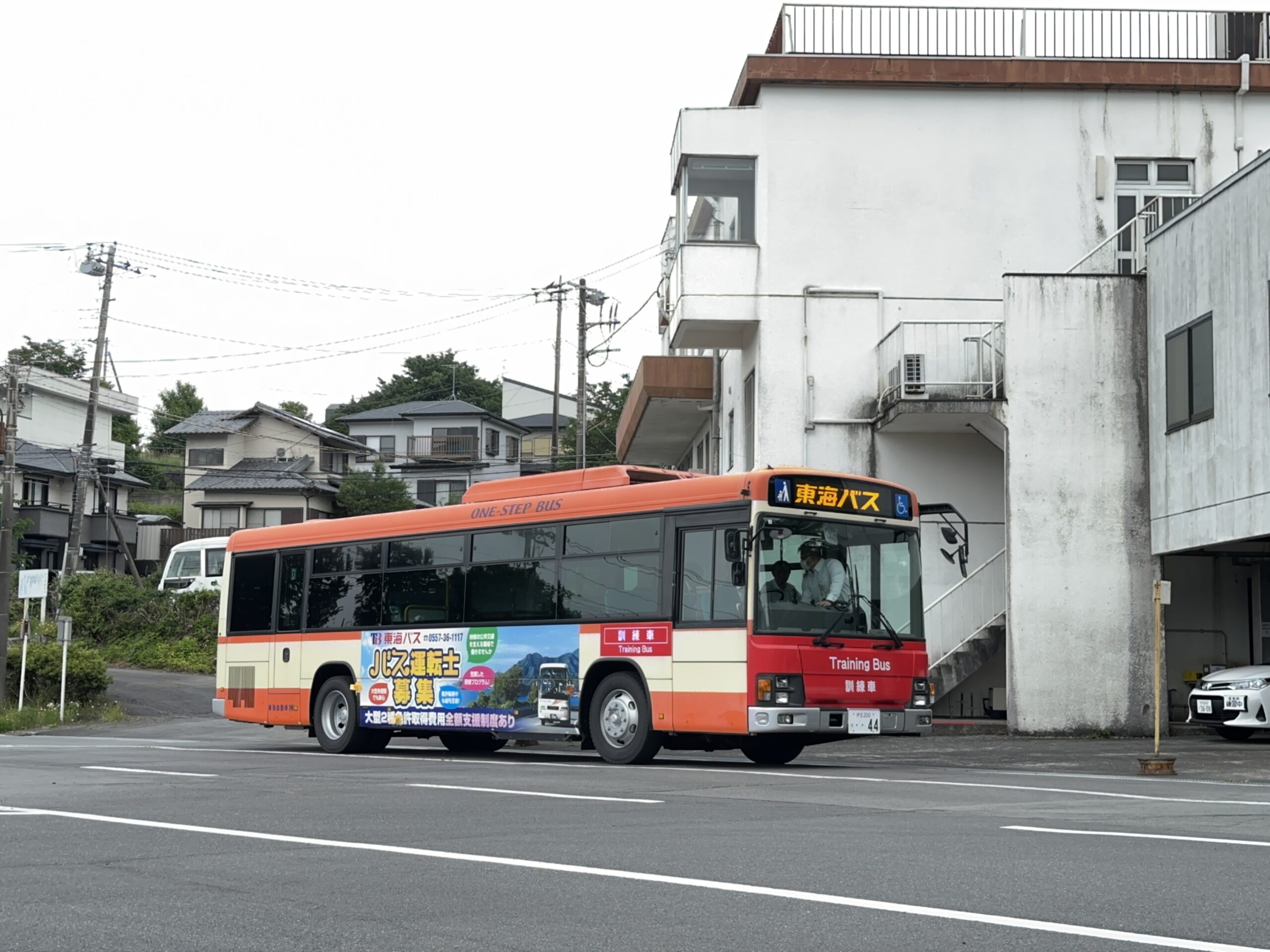敷地内で実際のバスの運転席に座り笑顔で操作を体験する未経験の30代男性、指導員が横で見守る、和やかで安心感のある雰囲気