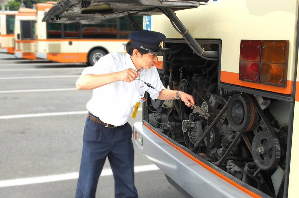 制服を着て明るい表情でバスの乗務前点検を行う未経験入社の男性運転士、先輩スタッフが横で丁寧に指導している様子