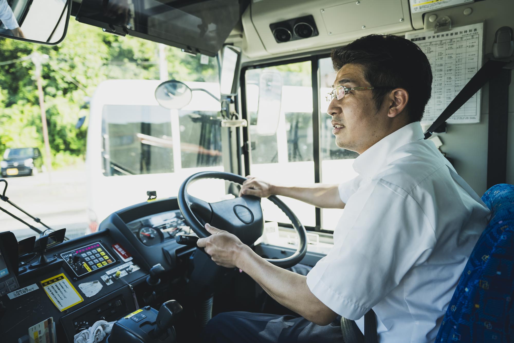 地方の路線を走る大型路線バスと、運転席で誇らしげな表情を見せるバス運転士
