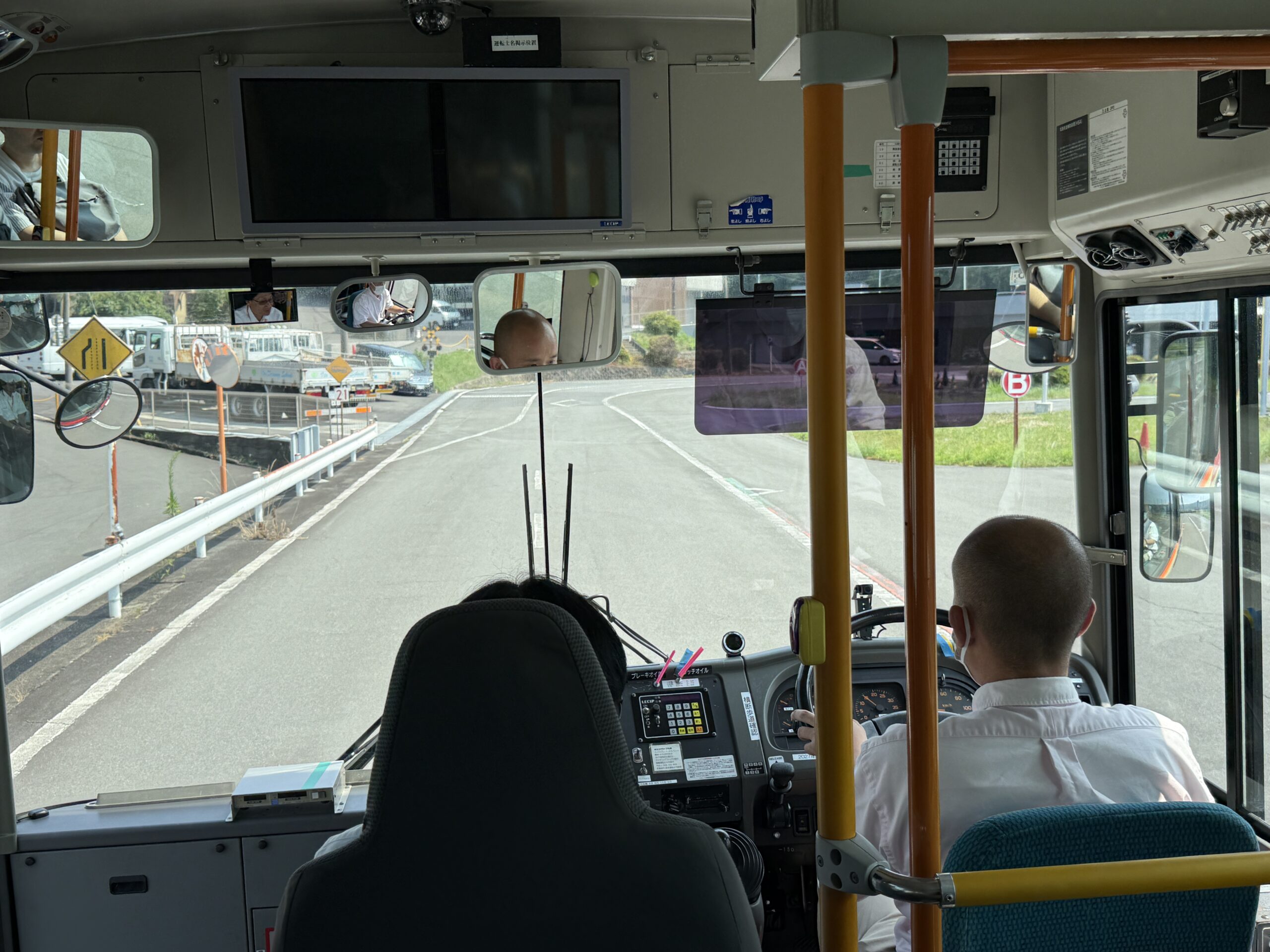 敷地内でバスの運転席に座り、初めての運転に驚きと笑顔を見せる私服姿の体験参加者