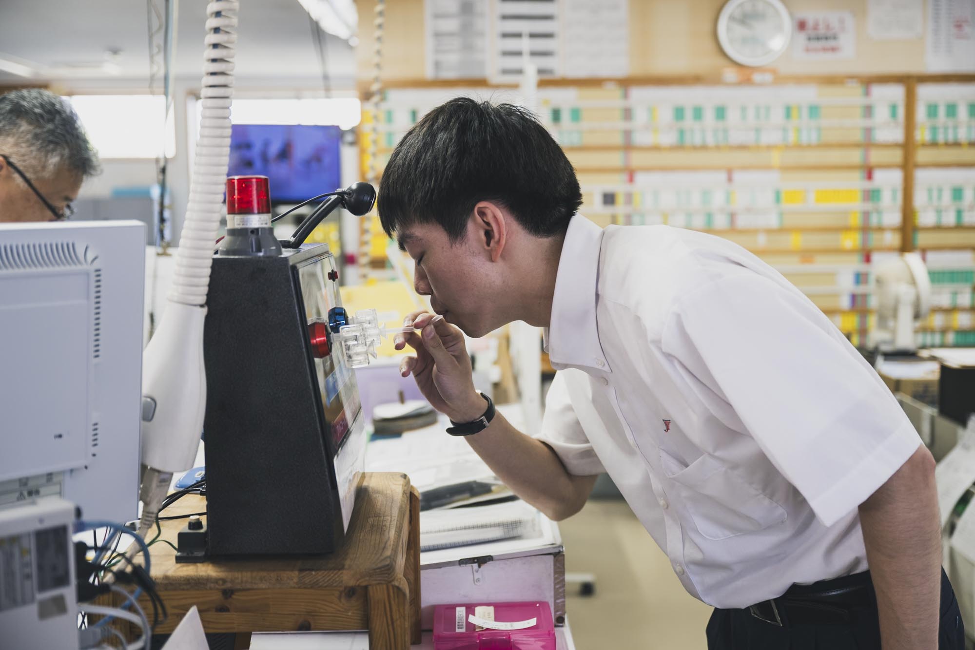 早朝の営業所でアルコール検知器に息を吹き込み、真剣な表情で検査を受けるバス運転士の男性