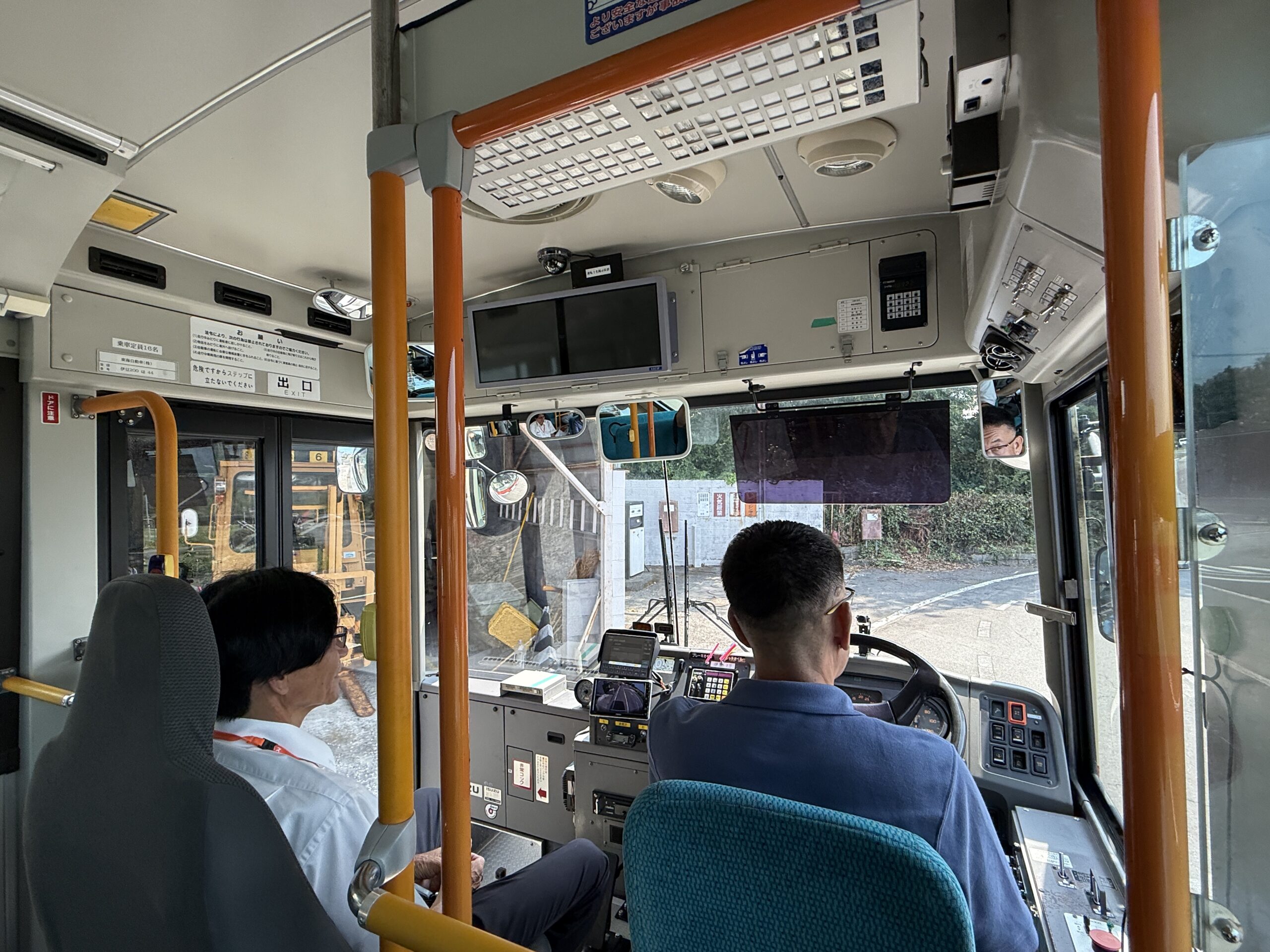 敷地内でバスの運転席に座り、初めての運転に驚きと笑顔を見せる私服姿の体験会参加者