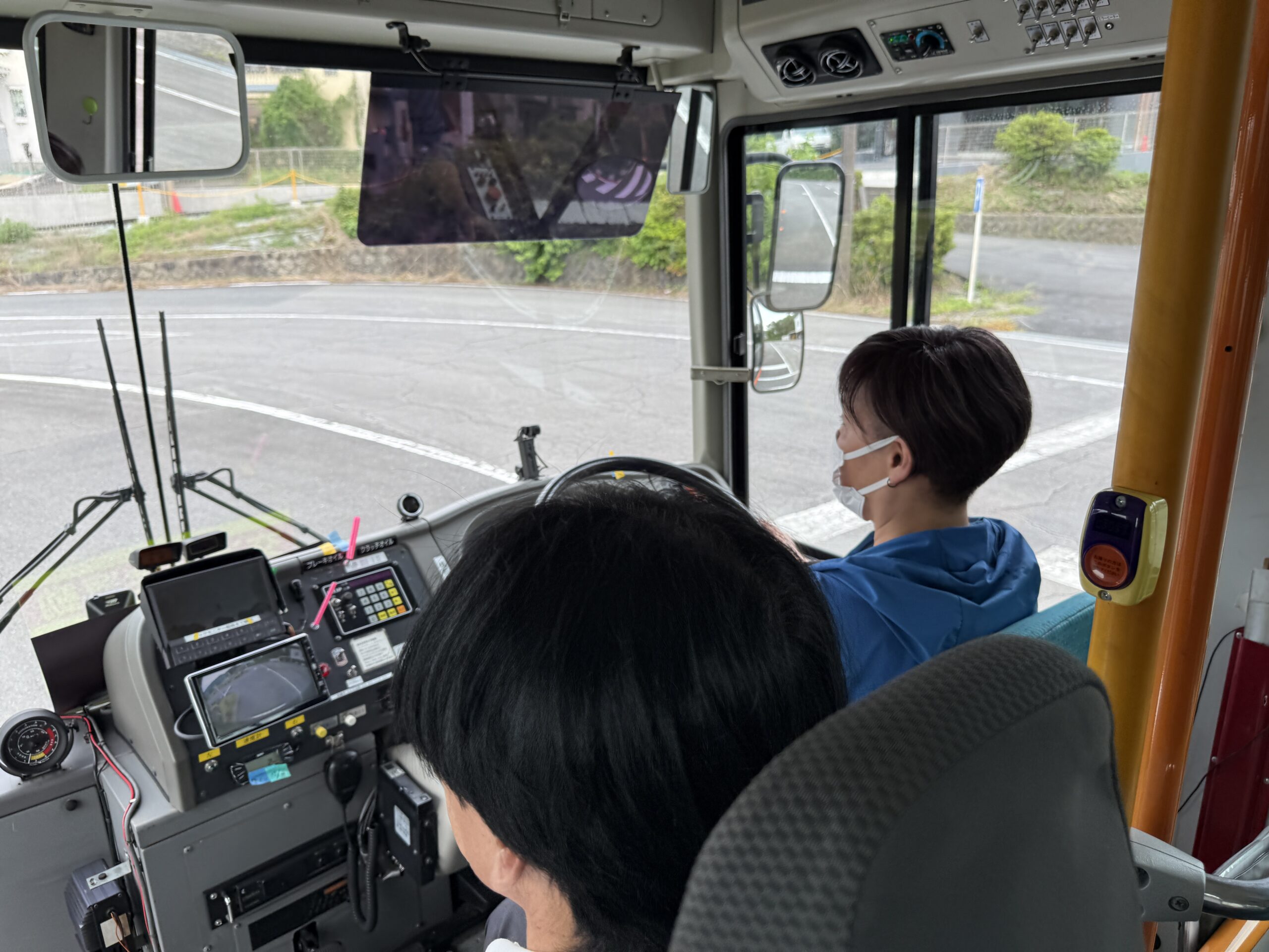 敷地内でバスの運転席に座り、初めての運転に驚きと笑顔を見せる私服姿の体験参加者